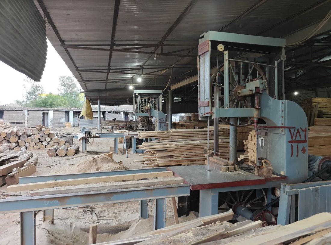 Band saw in the Man Impex sawmill, with teak logs and sawn planks behind it